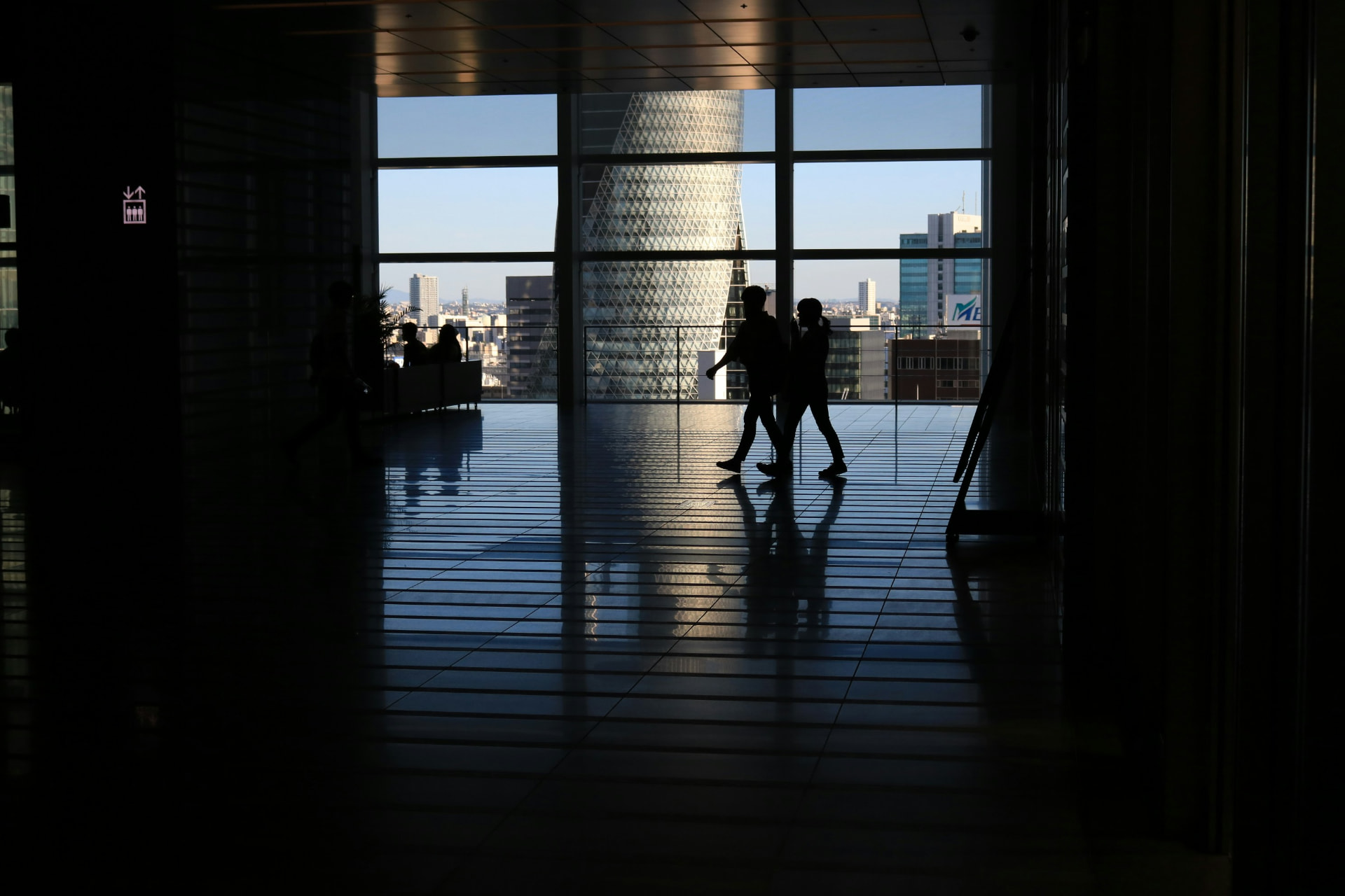 Silhouetted figures walking past floor to ceiling windows overlooking a city skyline